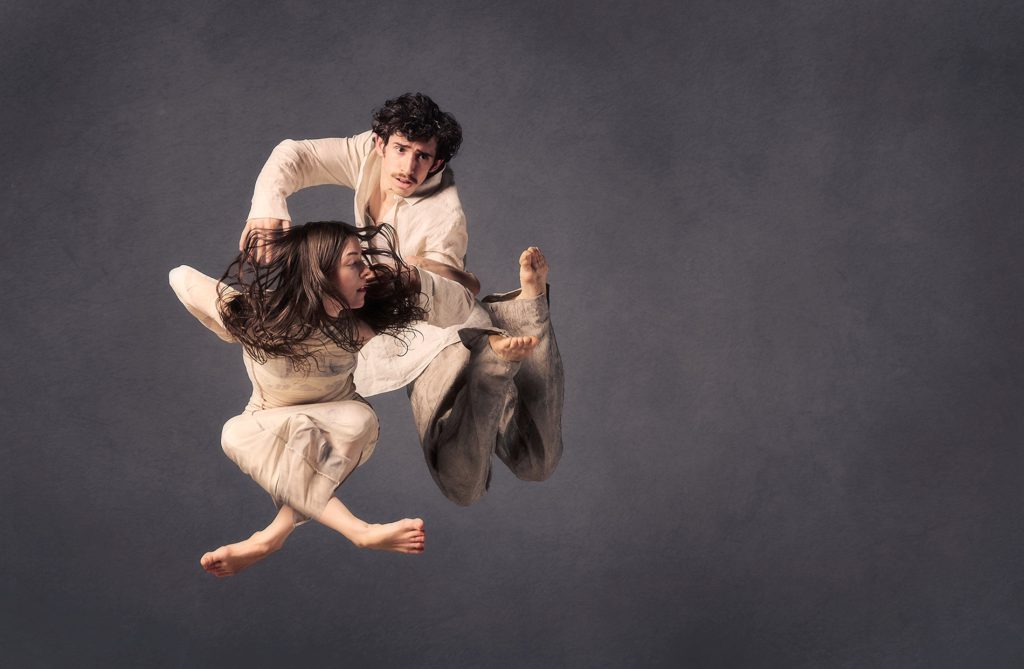 Two people hover in mid-air, performing a dance in motion against each other as they fly freely. The background is dark blue and blurred, focusing on the two contending figures. It's an intense snapshot of a thrilling dance.